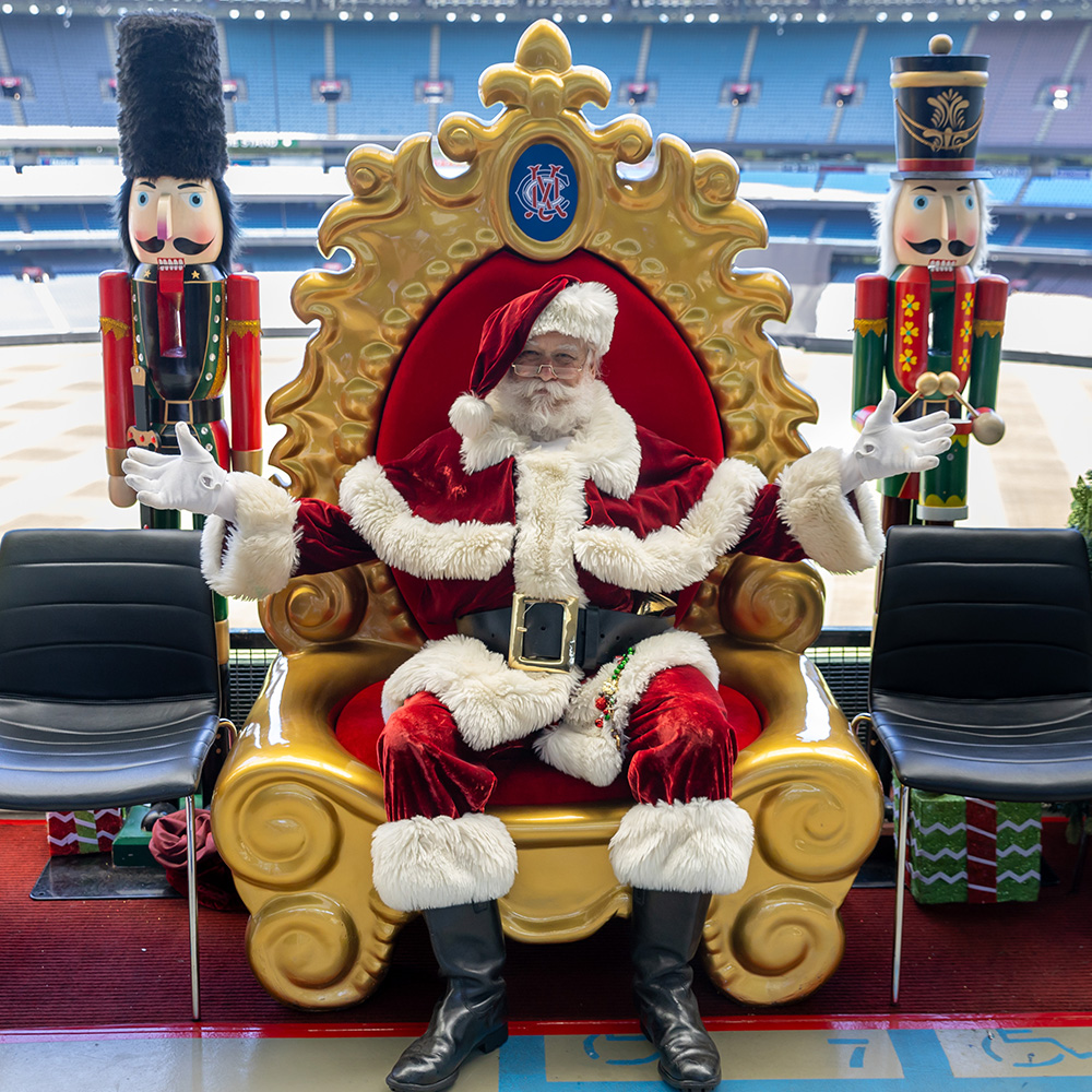 Santa sits on a chair on Level 4 of the MCG with the arena in the background