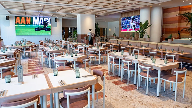 Tables set for service in dining room with natural light and screens showing sport