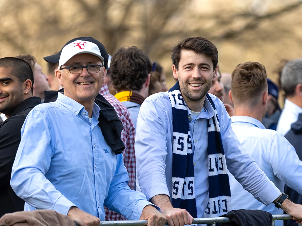 Smiling AFL fans lean on barrier waiting to enter MCC