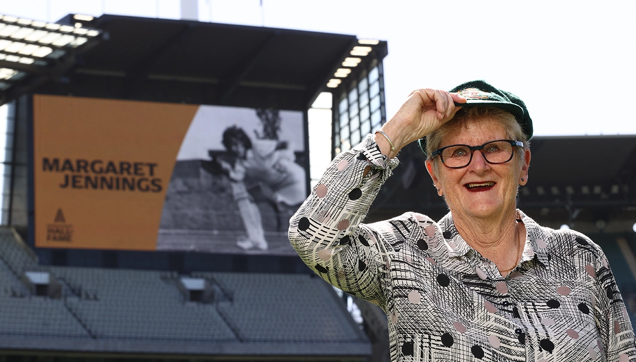 Australian Cricket Hall of Fame inductee Marg Jennings stands in in front of the MCG big screen wearing her baggy green cap Marg Jennings_2_MCC page banner desktop_1280x729.webp