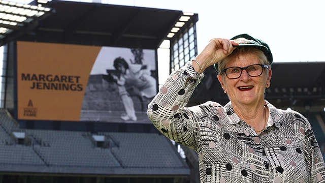 Australian Cricket Hall of Fame inductee Marg Jennings stands in in front of the MCG big screen wearing her baggy green cap Marg Jennings_2_Preview Image Card_640x360.webp