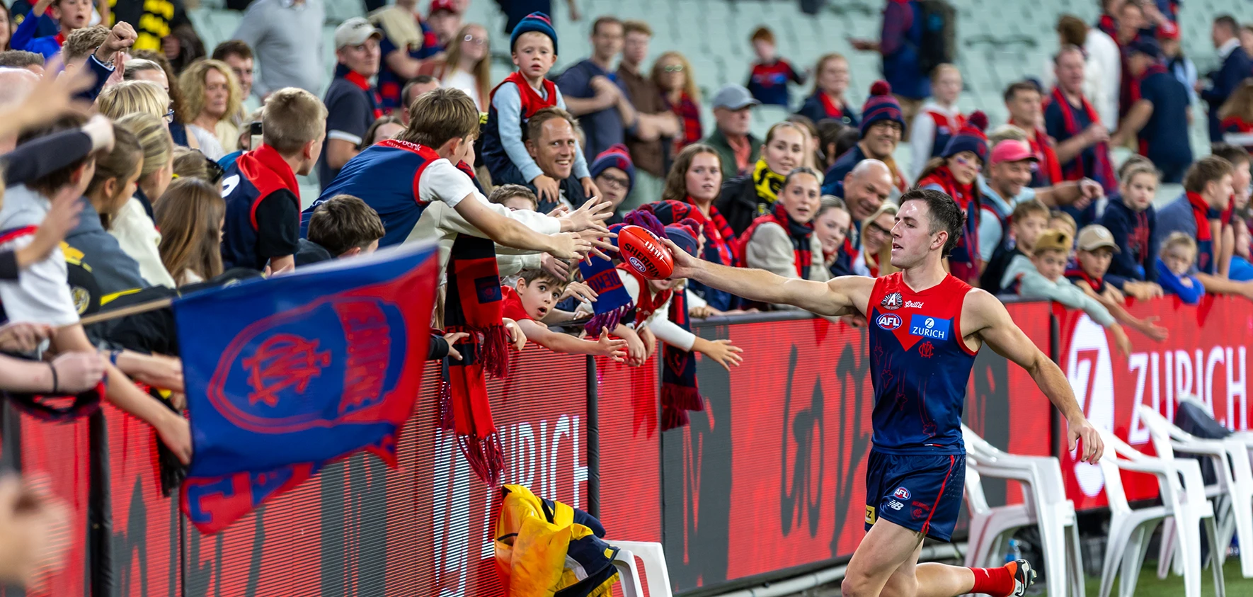 Melbourne Demons player hands footy to fans on the boundary