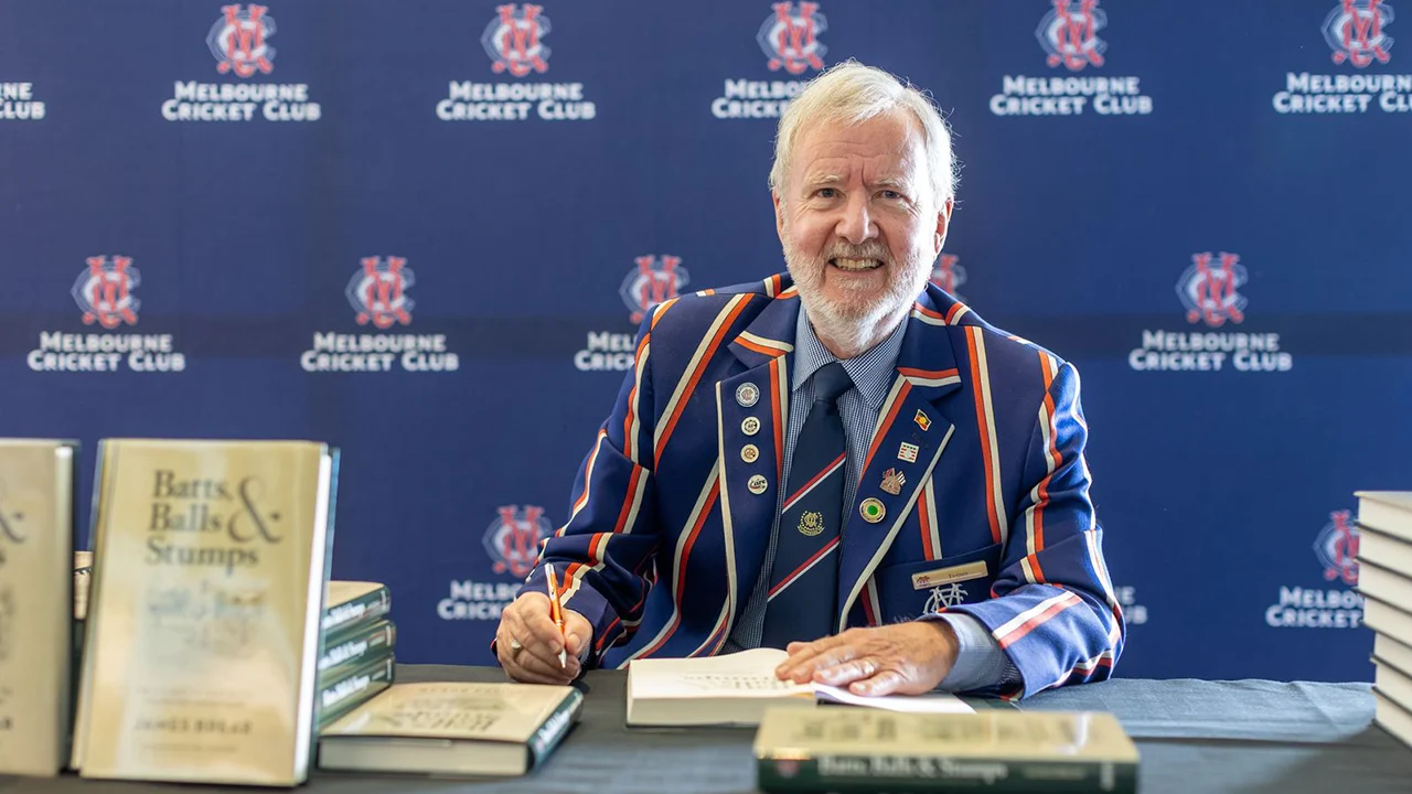 James Brear signs books in front of MCC logo wall