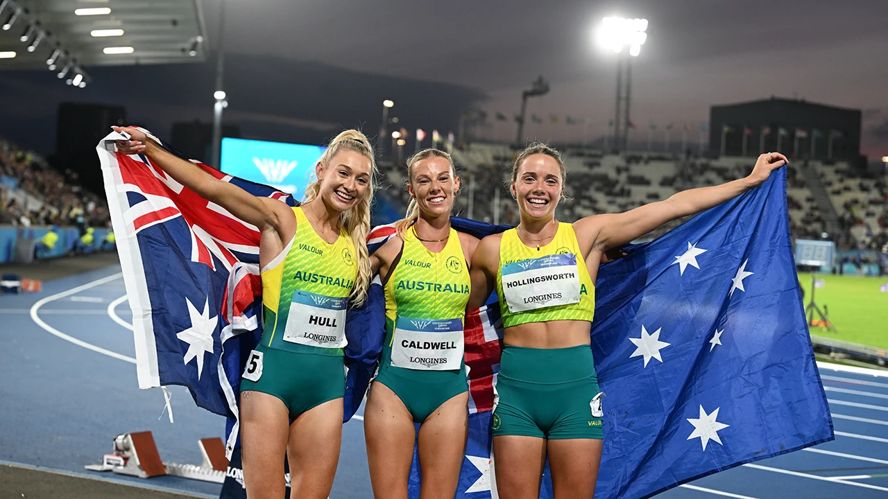 Team Australia medal winners celebrate on the athletics track: Abbey Caldwell, Jessica Hull and Claudia Hollingsworth