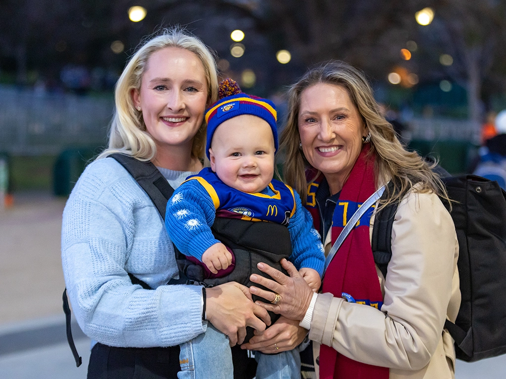 Two women and a baby in Brisbane Lions merchandise outside the MCG AFL25QF2_GEELv_BRIS_062_MCC CTA desktop_1024x768.webp
